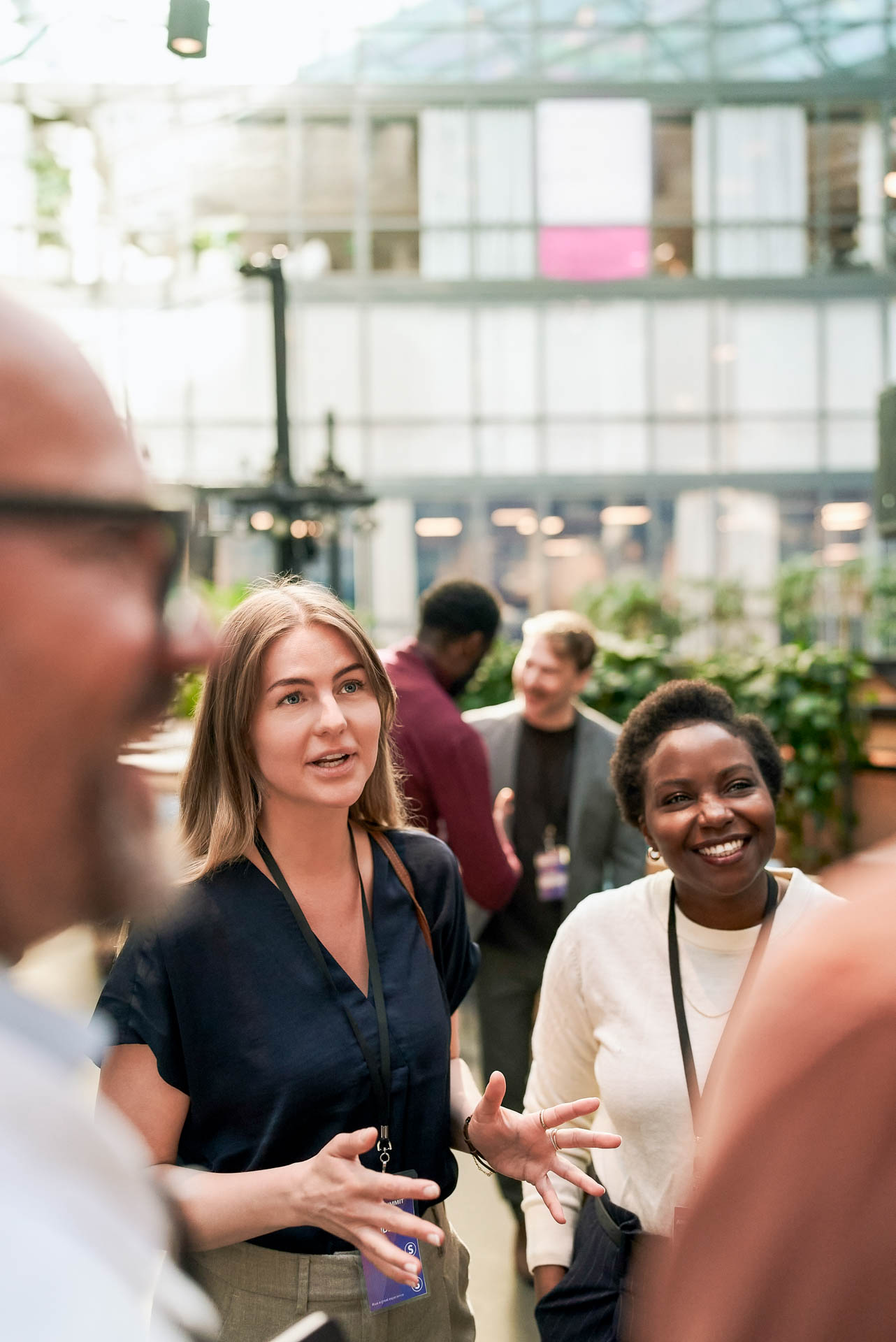 Smiling Businesswoman Standing Beside Colleague Exchanging Ideas With People Regarding Connectioneering During Event At